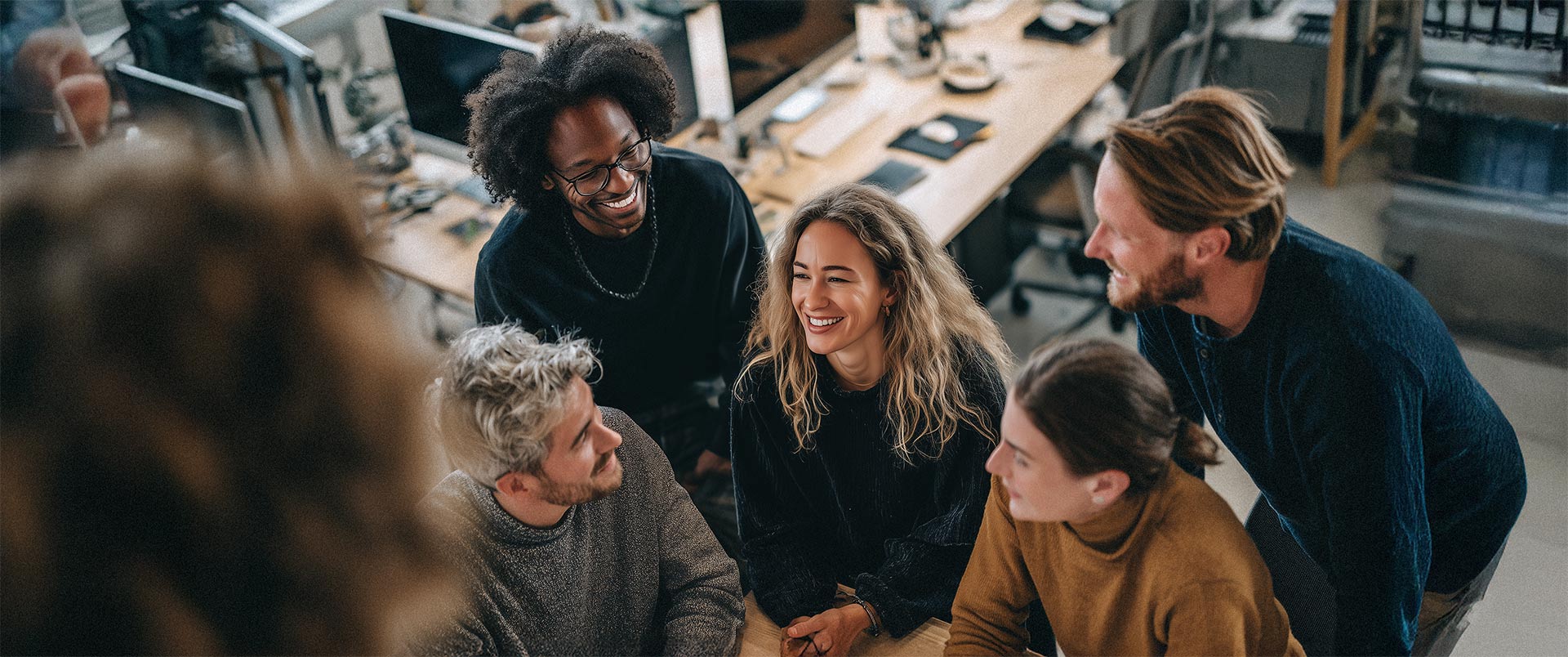Team im kreativen Austausch an Arbeitsplätzen, lachend und engagiert – Symbol für Ideenreichtum und Teamdynamik im HR Marketing.